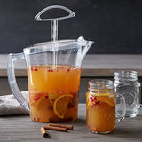 Clear, BPA-free stirring pitcher with orange juice and fruit, next to a glass jar filled with the same drink on a wooden surface.