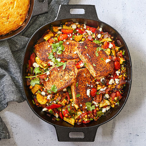 Large, black cast iron skillet with handles filled with seasoned chicken and vegetables.