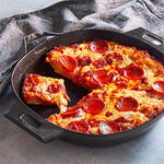 Pepperoni pizza in a cast iron skillet with one slice removed on a gray surface.