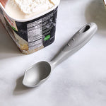 Gray ice cream scoop next to a container of ice cream on a white surface.