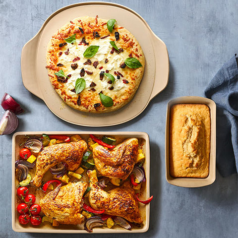 Three dishes of food including a pizza, roasted chicken with vegetables, and a loaf of bread in Stoneware Starter Set.