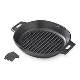 Black cast iron grill pan with handles on a white background and grill scraper to the side.