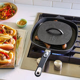 Black cast iron skillet, with grill press, on a stove with sausages cooking, next to a plate of hot dogs and vegetables.
