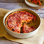 Quiche with a slice removed, placed in Stoneware Round Baker dish on a wooden surface.