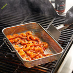 Shrimp being cooked in a mesh pan on a grill with a bottle of sauce in the background.