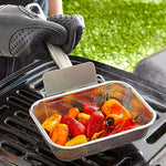 Vegetables being grilled using a mesh basket on a barbecue grill.