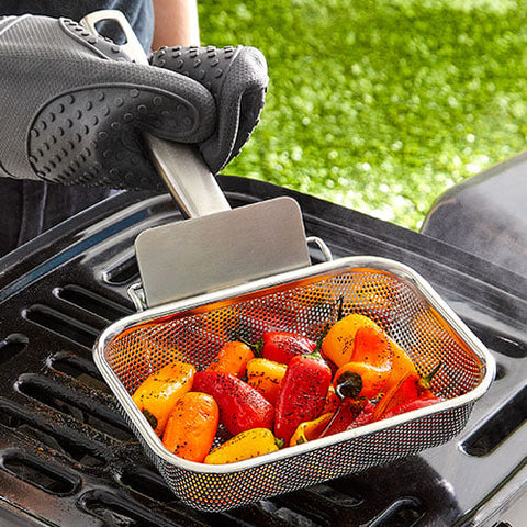 Vegetables being grilled using a mesh basket on a barbecue grill.