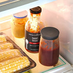 Two bottles of sauces in kitchen refrigerator with corn on the cob.
