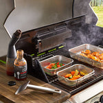 Outdoor grill with food being cooked, including vegetables and a bottle of sauce.