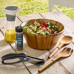 Wooden salad bowl with salad, dressing, and utensils on a wooden table outdoors.