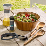 Wooden salad bowl with salad, dressing, and utensils on a wooden table outdoors.