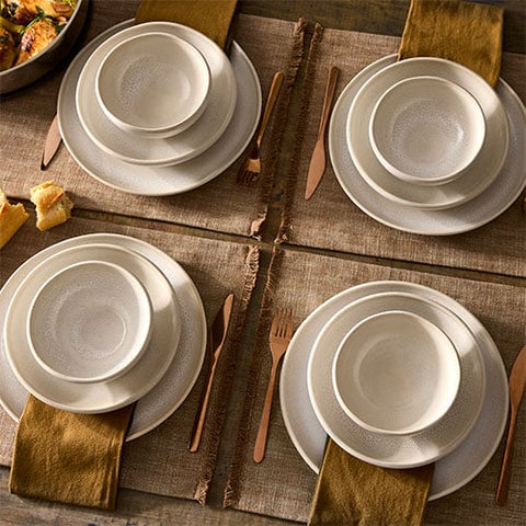 Set of white ceramic dinnerware set, along with gold cutlery on a wooden table.