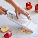 Person using a mandoline slicer to slice apples on a white surface.