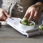 Person using a white mandoline slicer to slice Brussels sprouts into a bowl.