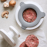 Hamburger press with ground meat and hamburger patties on a light surface