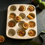 12-Cup Stoneware Muffin Pan with mini pies on a wooden surface.