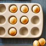 12-Cup Stoneware Muffin Pan with baked muffins on a textured surface.