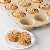 12-Cup Stoneware Muffin Pan with two muffins on a plate on a marble surface.