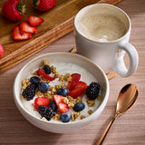 Coffee mug with warm beverage, along with cereal bowl containing cereal and fruit.
