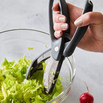 Hand using kitchen shears to cut lettuce in a glass bowl on a light surface.