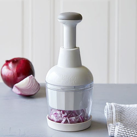 Handheld, manual food chopper with chopped red onions on a kitchen counter.