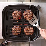 Hamburgers being cooked on a portable grill with a spatula.
