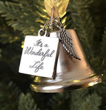 Silver bell ornament with 'It's a Wonderful Life' tag and angel wing charm on a Christmas tree.