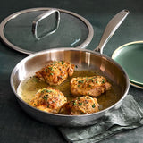 Stainless Steel Cookware pan with cooked chicken and lid, plates, along with napkin to the side.