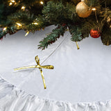 Gold bow ornament on a white surface with a Christmas tree in the background