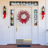 White front door with a red wreath and bows, flanked by two lanterns with red bows on a white house exterior.