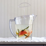 Clear, BPA-free stirring pitcher with fruit and herbs in water on a white surface.