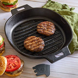 Two burgers in 12" (30cm) Cast Iron Grill Pan Skillet on a wooden surface with a green towel to the side.