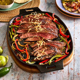 Steak with peppers and onions in a cast iron skillet on a wooden trivet board.