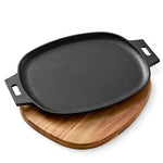 Black cast iron griddle with handles on a wooden trivet board against a white background.