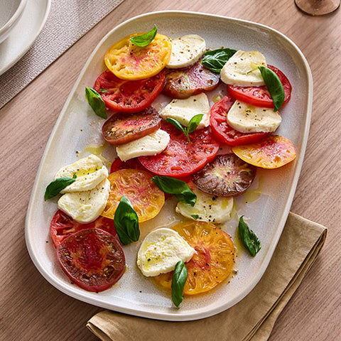 Rectangular Ceramic Serving Platter of sliced tomatoes and mozzarella with basil on a wooden table.