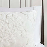 Close-up of a textured white pillow on a bed with a neutral headboard.