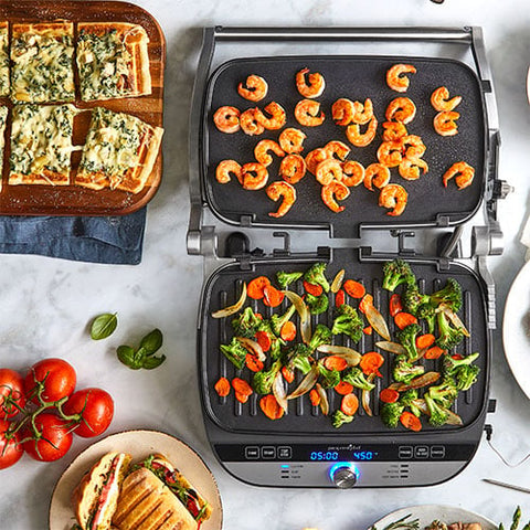 Multifunctional, Deluxe Electric Countertop Grill and Griddle with food on a marble countertop.