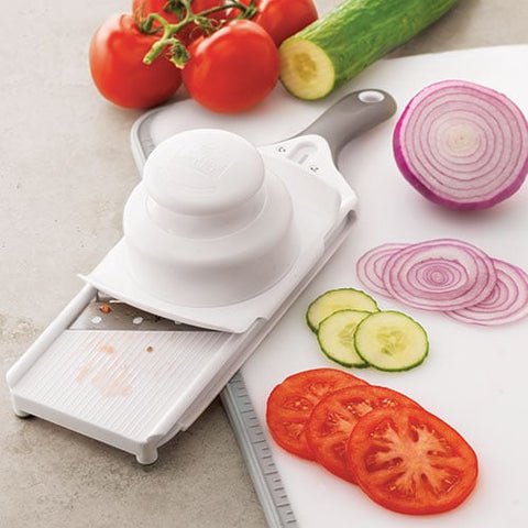 Handheld food mandoline with sliced vegetables on a cutting board.