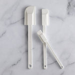 Three white kitchen spatulas on a marble surface.