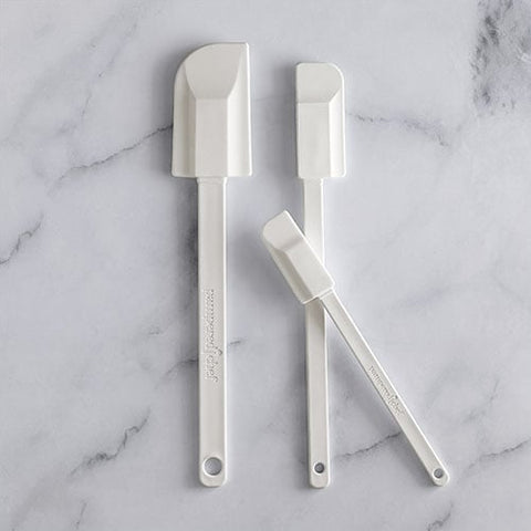 Three white kitchen spatulas on a marble surface.