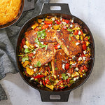 Large, black cast iron skillet with handles filled with seasoned chicken and vegetables.