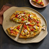 Vegetable pizza on a beige, large round pizza stoneware with a slice removed, on a dark surface.