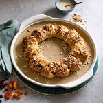 Pastry wreath on a large, round pizza stoneware dish with a bowl of icing in the background.