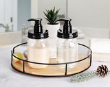 Two BPA-free, plastic glass jars with black pumps on a round wooden tray in a bathroom setting.