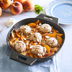Black, medium-sized, cast iron skillet with peach cobbler and vanilla ice cream on a light blue tablecloth.
