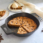 Black, cast iron skillet with giant-sized cookie served with ice cream on a light surface.