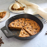 Black, cast iron skillet with giant-sized cookie served with ice cream on a light surface.