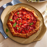 Tomato galette on a beige, medium pizza stone plate with a blue napkin.