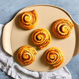 Five cinnamon rolls on medium pizza stone plate with a blue background.