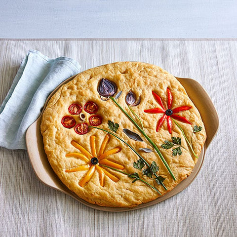 Decorative pizza with vegetable flowers on a medium pizza stoneware with two handles. 